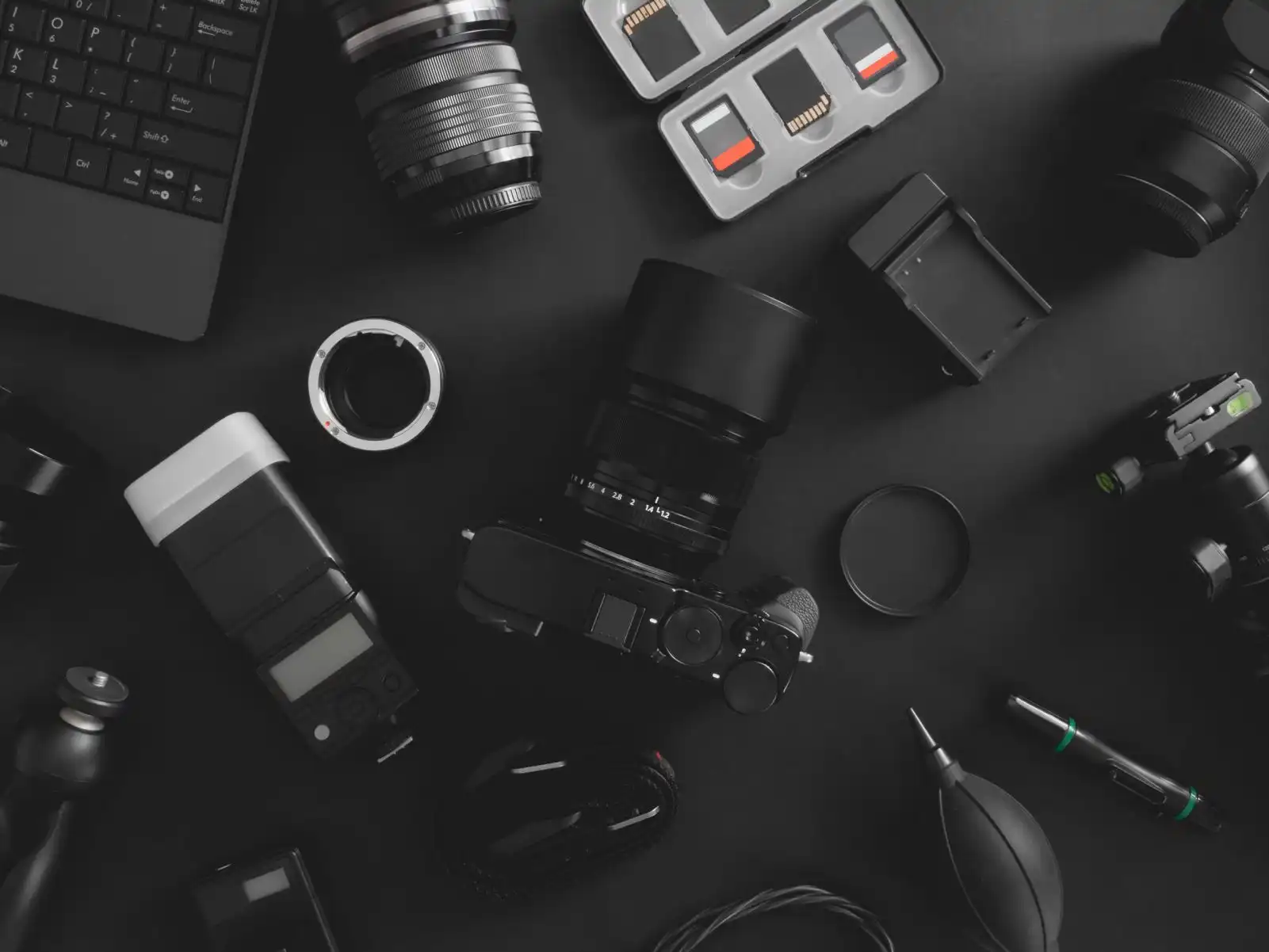 Draufsicht auf den Arbeitsplatz des Fotografen mit Digitalkamera, Blitz, Reinigungsset, Speicherkarte, Stativ und Kamerazubehör auf schwarzem Tischhintergrund